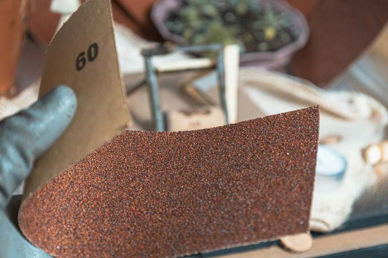 Workspace with various sandpaper types laid out beside wood samples and sanding blocks